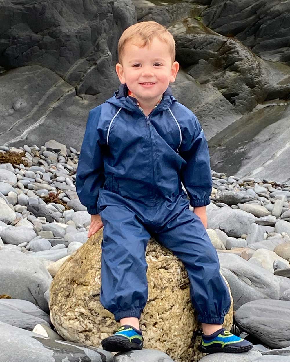 Navy coloured Fort Childrens Splashaway Rainsuit on rocky background