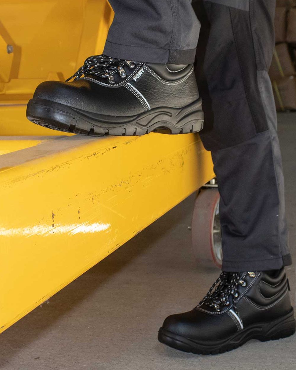 Black coloured Fort Workforce Safety Boots on warehouse background