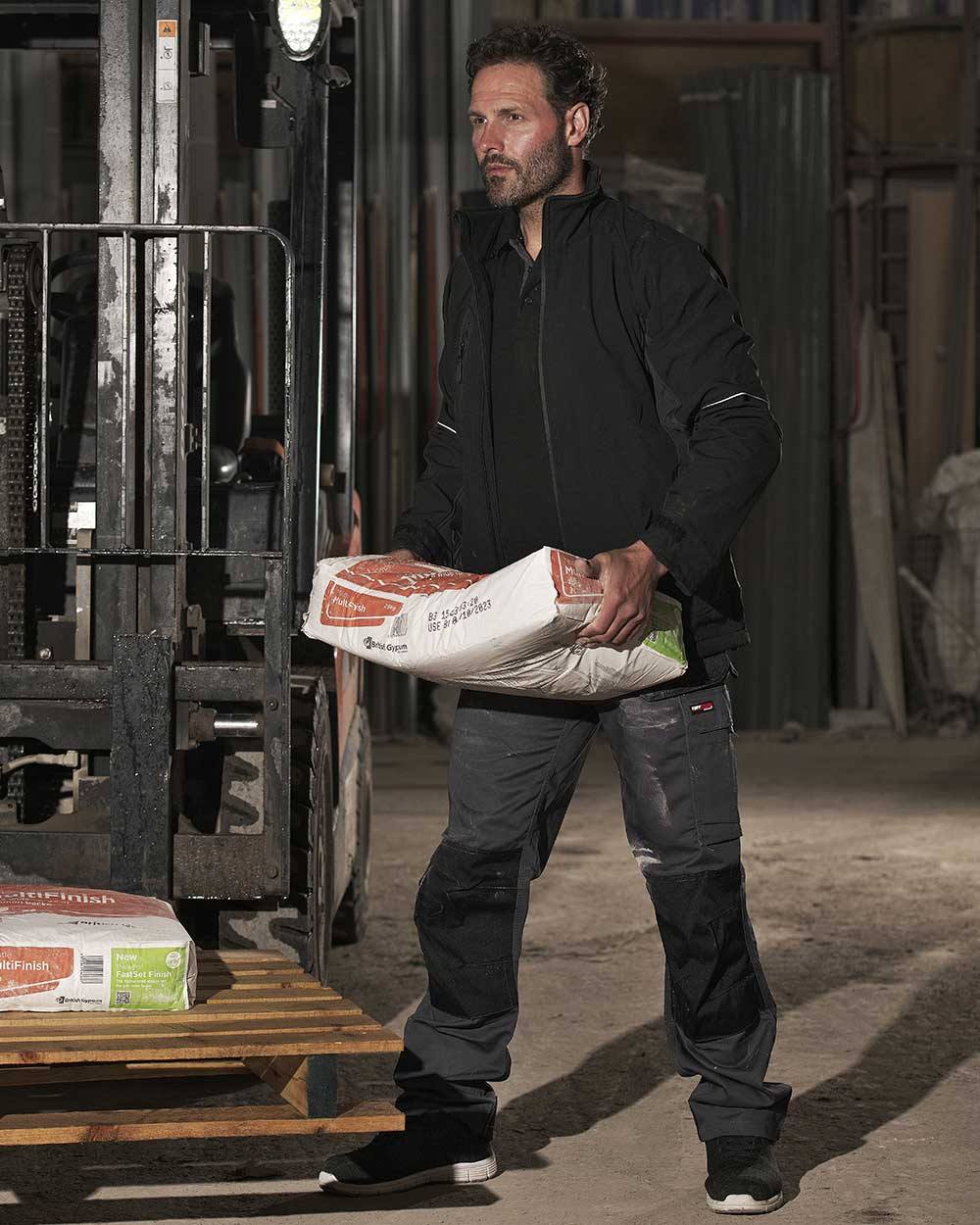 Grey Coloured TuffStuff Excel Work Trousers On A Warehouse Background