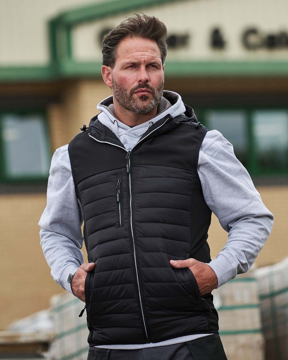 Black Coloured TuffStuff Howden Hooded Bodywarmer On A Warehouse Background