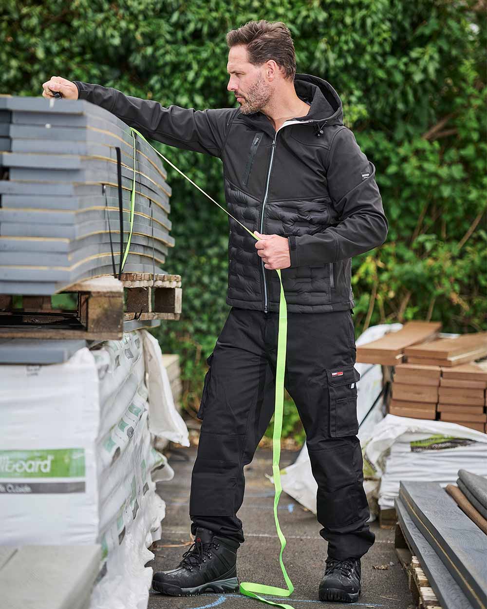 Black Coloured TuffStuff Pro Work Trousers On A Warehouse Background 