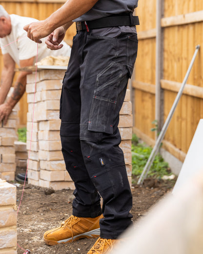 Black coloured TuffStuff Evo Flex Trousers with construction background