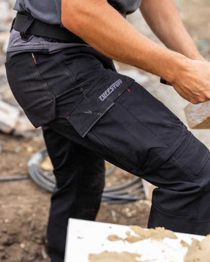 Black coloured TuffStuff Evo Flex Trousers with construction background