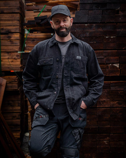 Man wearing a Black TuffStuff Cap and Black coloured TuffStuff Ranger Jacket with a lumber yard background 