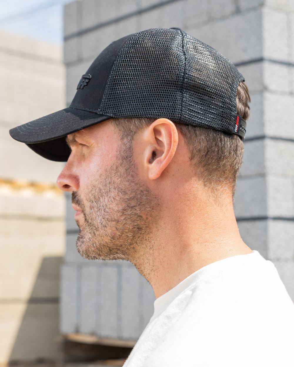 Black coloured TuffStuff Trucker Cap on construction background 