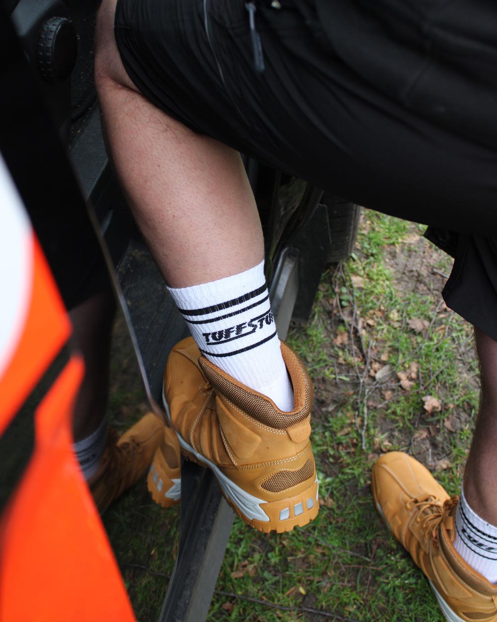 Person wearing brown boots and white TuffStuff crew socks, stepping into  work van.